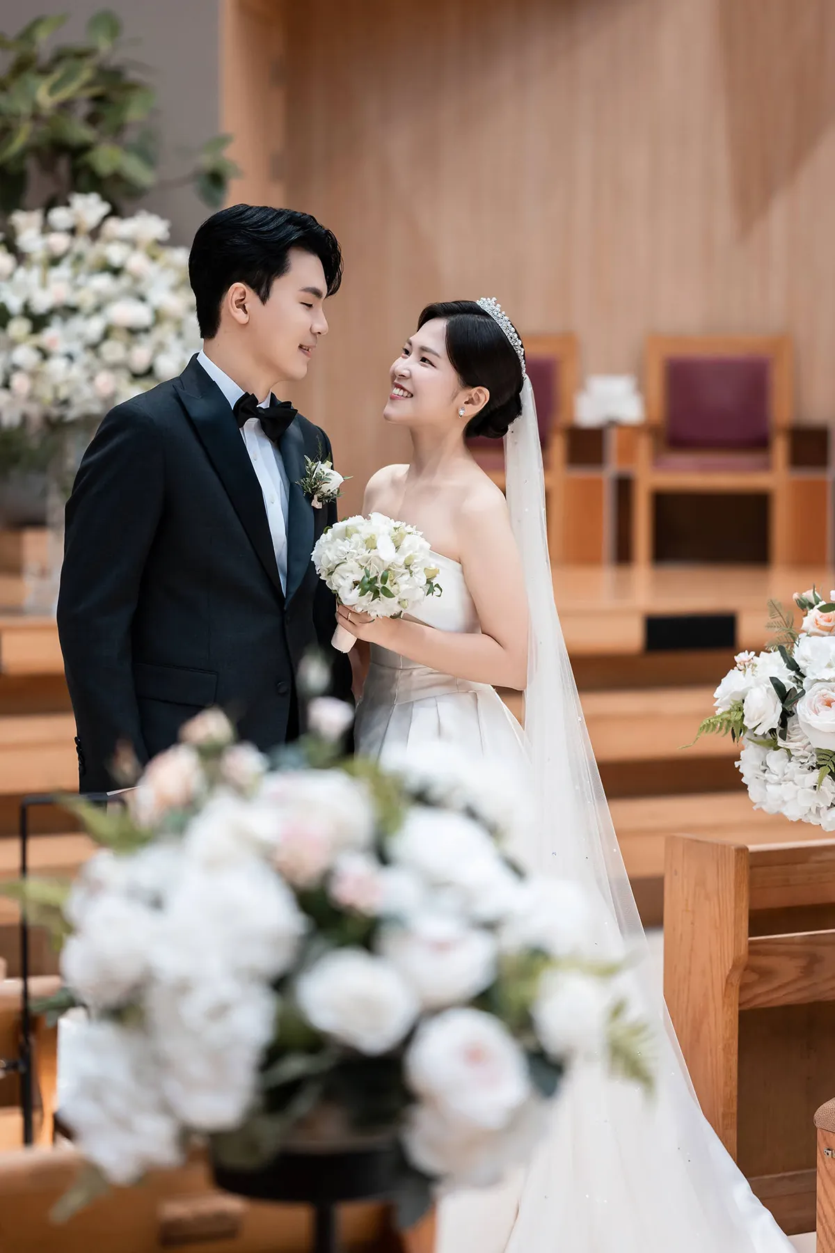 예배당 꽃장식 앞에서 서로 바라보며 웃는 신랑신부의 교회웨딩 스냅